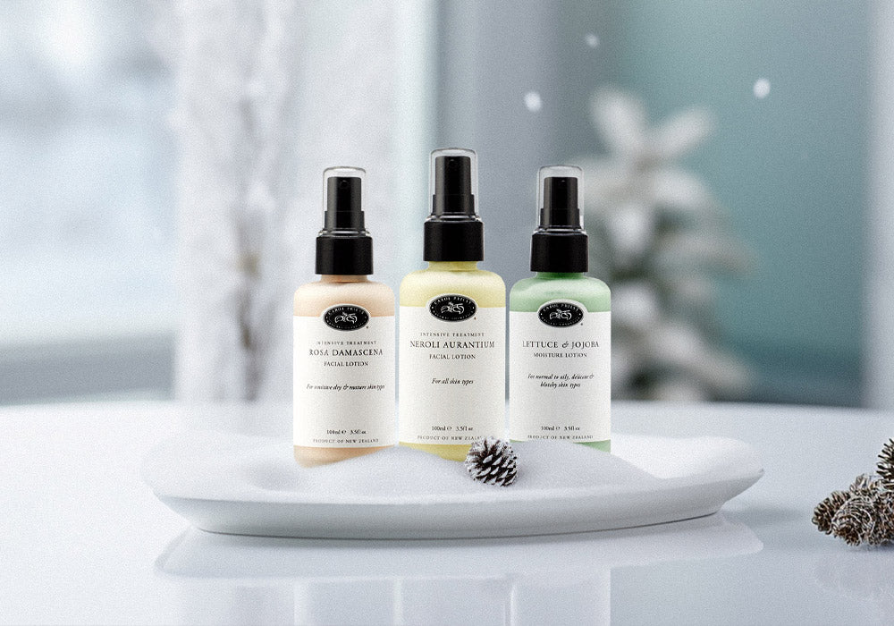 A collection of Carol Priest's vegan lotions arranged on a snow-covered plate within a cozy Christmas ambiance amid falling snowflakes.